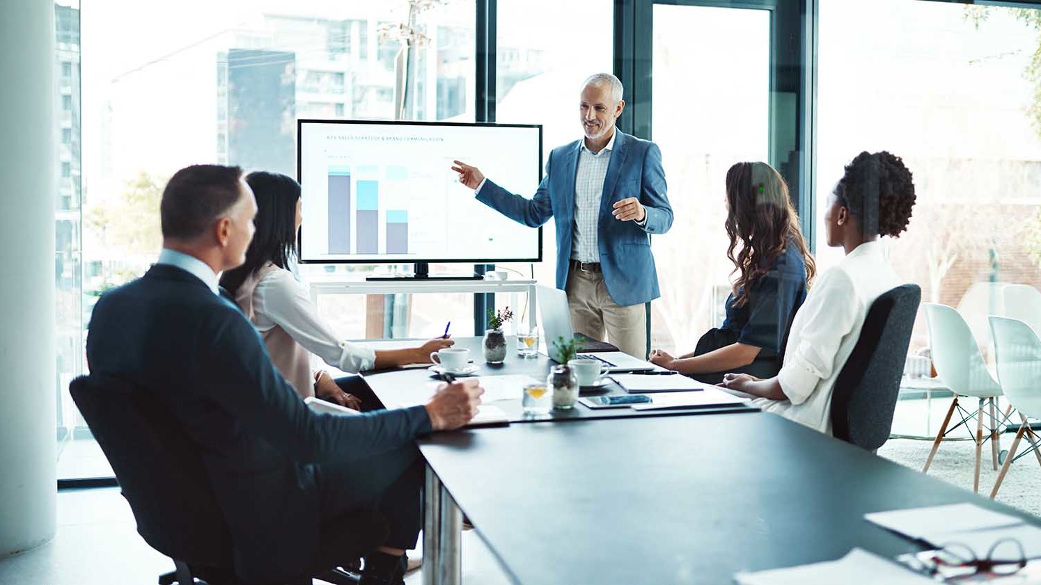 four people listening to a presentation, the presentor is referring to a chart
